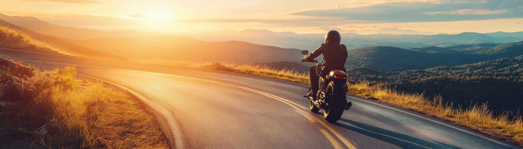 Un motard sur une route de montagne devant un coucher de soleil